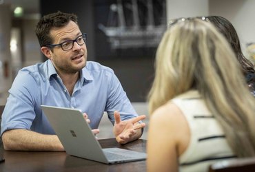 A man speaks to two women in front of a laptop