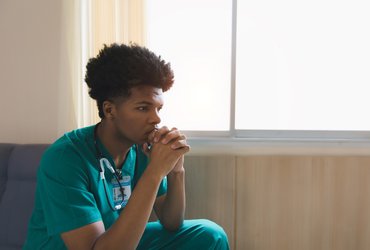 A young burnt out doctor sits resting his chin on his hands.