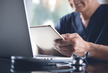 A man in scrubs intently using a tablet computer in a clinical setting.