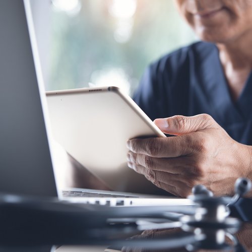 A man in scrubs intently using a tablet computer in a clinical setting.