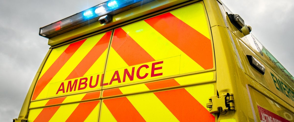 Close-up view of the back doors of an ambulance, against a grey sky. The blue emergency lights are switched on.