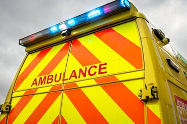 Close-up view of the back doors of an ambulance, against a grey sky. The blue emergency lights are switched on.