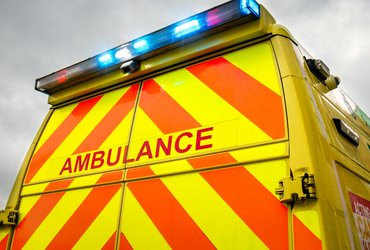 Close-up view of the back doors of an ambulance, against a grey sky. The blue emergency lights are switched on.