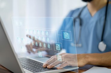 A doctor wearing blue scrubs uses a laptop. A graphic of computer folders to represent electronic patient record systems is superimposed on the photo.