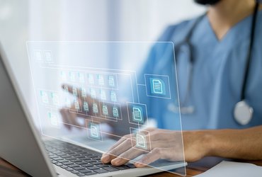 A doctor wearing blue scrubs uses a laptop. A graphic of computer folders to represent electronic patient record systems is superimposed on the photo.