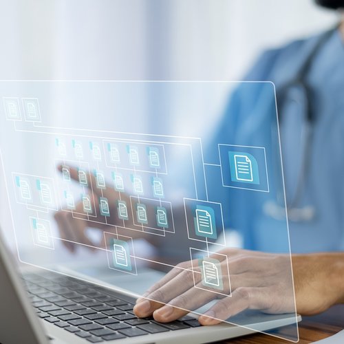 A doctor wearing blue scrubs uses a laptop. A graphic of computer folders to represent electronic patient record systems is superimposed on the photo.