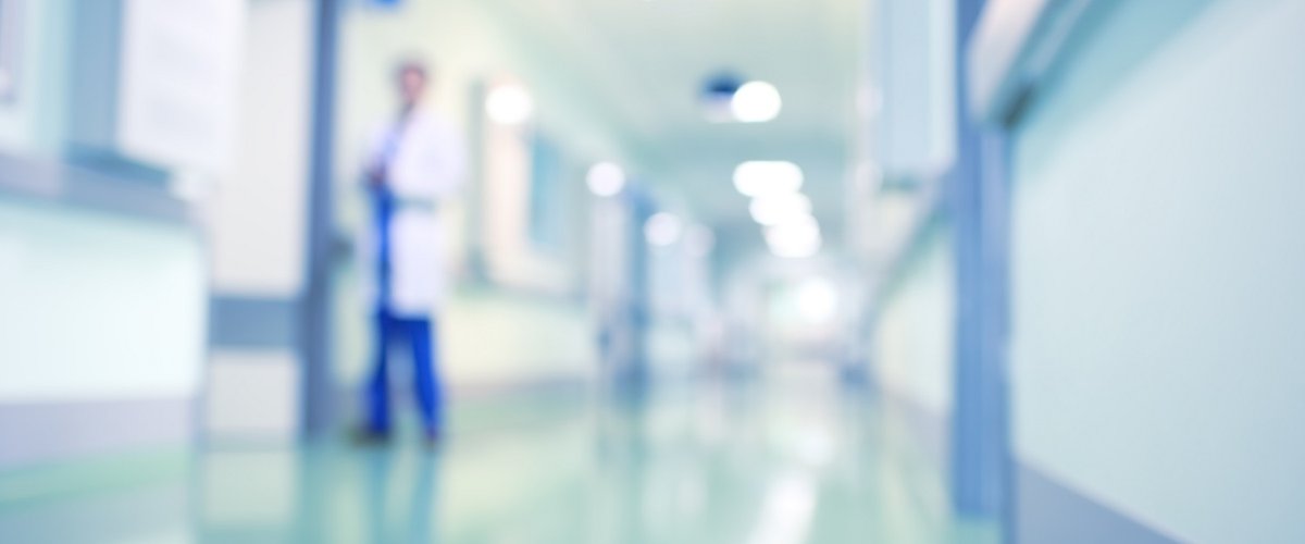 A doctor walks down a hospital corridor, the background and the doctor are blurred.