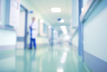 A doctor walks down a hospital corridor, the background and the doctor are blurred.