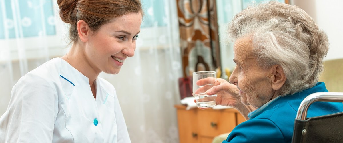 A female nurse gives an older woman medical pills.