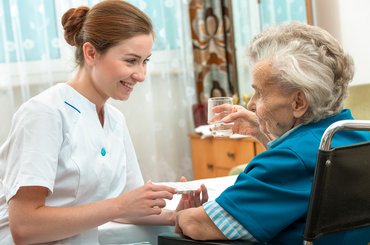 A female nurse gives an older woman medical pills.