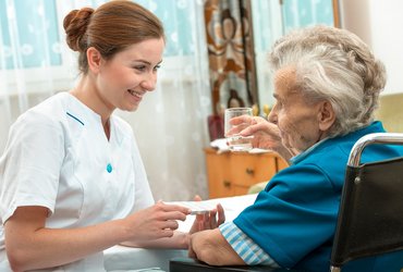 A female nurse gives an older woman medical pills.