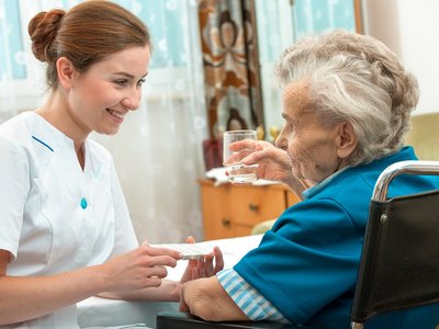 A female nurse gives an older woman medical pills.