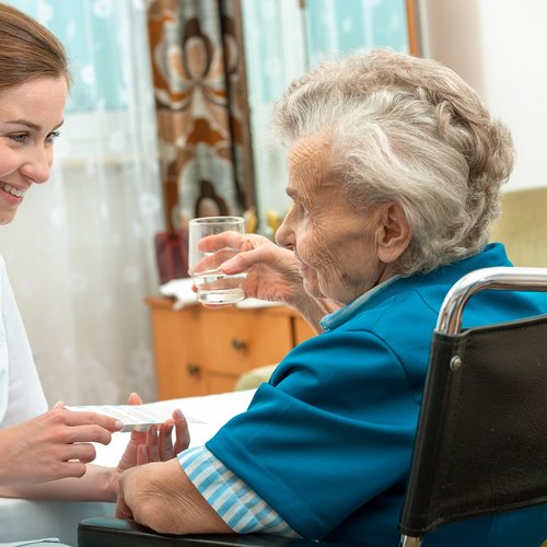 A female nurse gives an older woman medical pills.