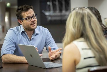 A man speaks to two women in front of a laptop