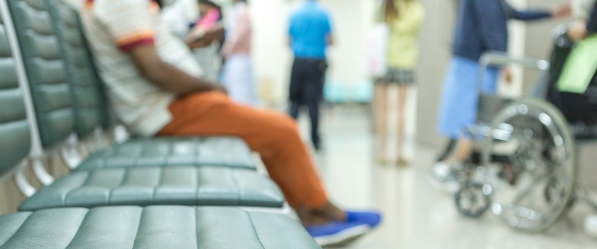 An image of a hospital waiting room with three empty seats and one seat occupied.