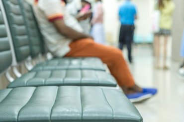 An image of a hospital waiting room with three empty seats and one seat occupied.