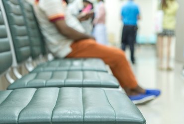 An image of a hospital waiting room with three empty seats and one seat occupied.