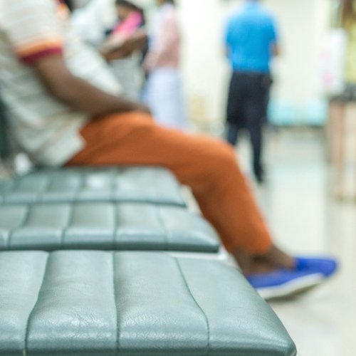 An image of a hospital waiting room with three empty seats and one seat occupied.