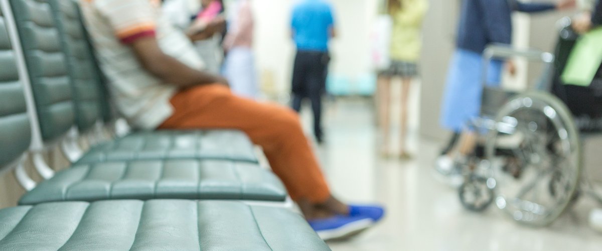 An image of a hospital waiting room with three empty seats and one seat occupied