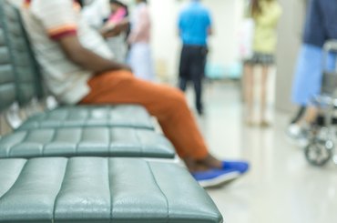 An image of a hospital waiting room with three empty seats and one seat occupied