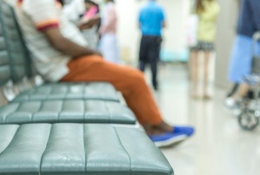 An image of a hospital waiting room with three empty seats and one seat occupied