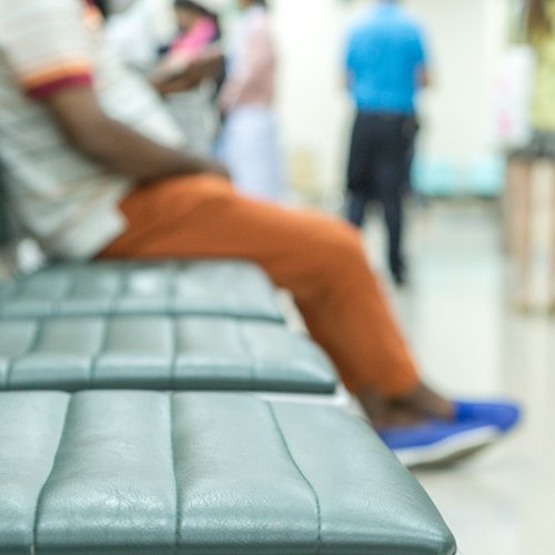An image of a hospital waiting room with three empty seats and one seat occupied