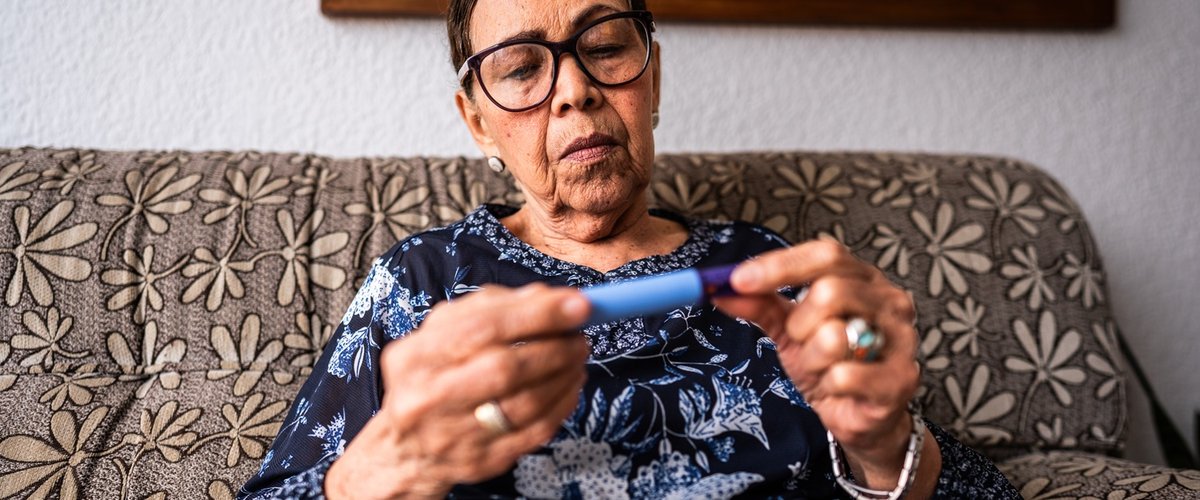 Person sitting on a patterned sofa at home, holding an insulin pen in both hands and checking it closely.