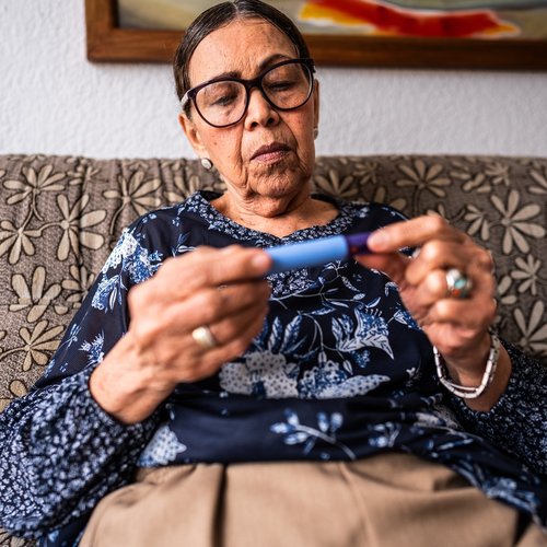 Person sitting on a patterned sofa at home, holding an insulin pen in both hands and checking it closely.