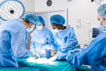 A surgical team wearing blue scrubs perform an operation in a hospital theatre.