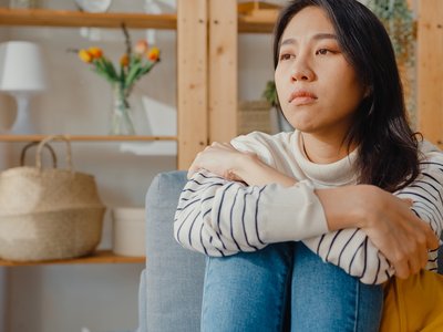A woman sits on a sofa hugging her knees.