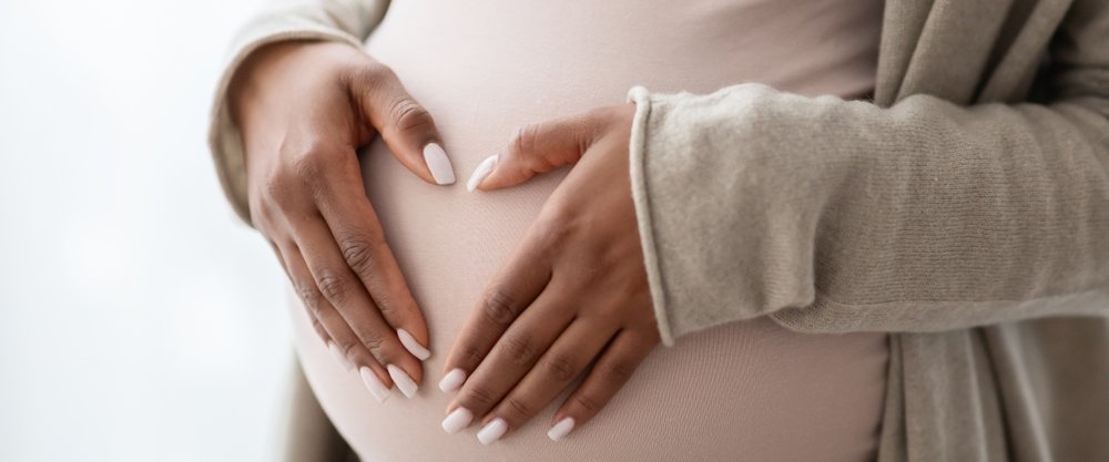 Image shows a pregnant person holding palms in a heart shape
