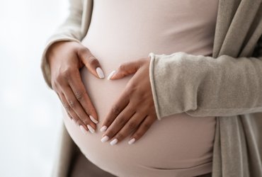 Image shows a pregnant person holding palms in a heart shape