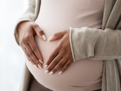 Image shows a pregnant person holding palms in a heart shape
