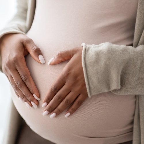 Image shows a pregnant person holding palms in a heart shape